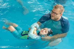 Baby swimming lesson with instructor supporting a relaxed back float in an indoor heated pool